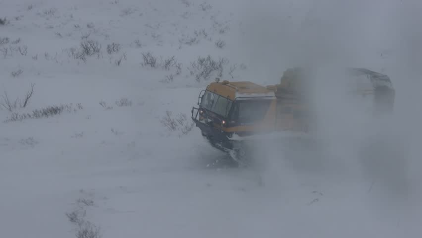 A tracked all-terrain vehicle travels through the winter tundra raising clouds of snow dust. Caterpillar truk (tracked-transport-snow-swamp vehicle)