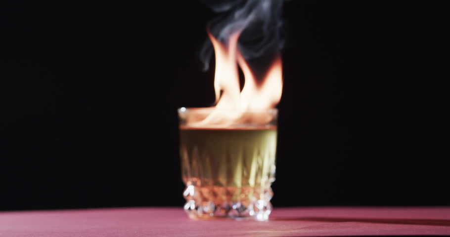 A flaming cocktail stands on a bar counter, creating a dramatic effect. Capturing the essence of mixology, this image showcases a bartender's flair and creativity, slow motion.