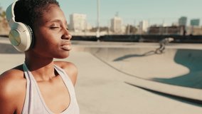 Close-up of young athletic woman sits in a skatepark on a hot summer day, with skateboarders performing tricks in the background, enjoys the music - Powered by Shutterstock - Get 15% off with code: PIKWIZARD15