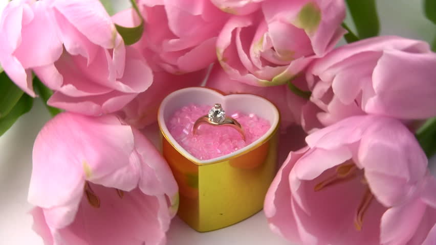A golden ring with precious stones in gift box as a heart, surrounded by fresh
