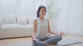 Happy young Asian woman practicing yoga and meditation at home sitting on floor in living room in lotus position and relaxing with closed eyes. Mindful meditation and wellbeing concept - Powered by Shutterstock - Get 15% off with code: PIKWIZARD15