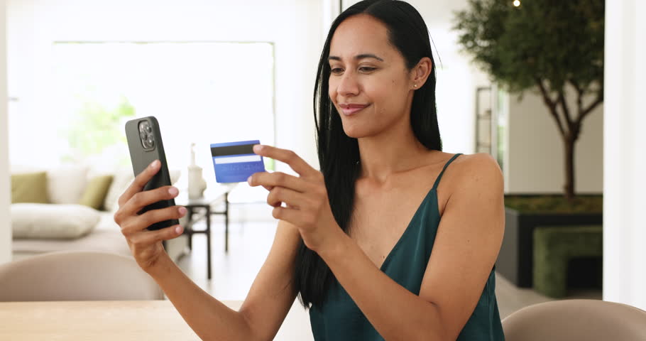 Smiling millennial woman sit indoors holding credit card and phone making purchase through mobile application, using marketplace websites, enjoy easy express e-services, transfer money via modern app