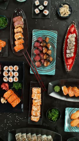 Top view of traditional japanese cuisine . Sushi rolls set with salmon , tuna fish and vegetable served on black stone table . Asian food on black stone slate with chopsticks . Camera movement .