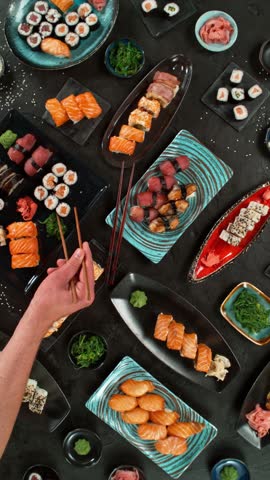 Top view of traditional japanese cuisine . Sushi rolls set with salmon , tuna fish and vegetable served on black stone table . Asian food on black stone slate with chopsticks . Camera movement .