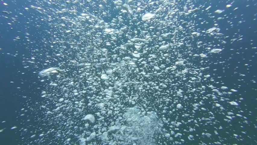 slow motion video with the camera going through oxygen bubbles rising while diving in the blue ocean