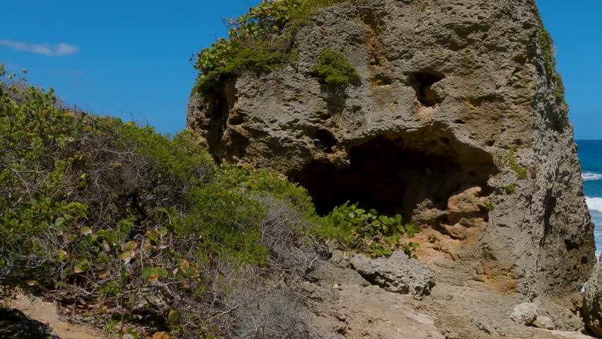 Rocky coastal landscape with waves crashing against large rocks under a clear blue sky at Aguadilla coast, Puerto Rico.