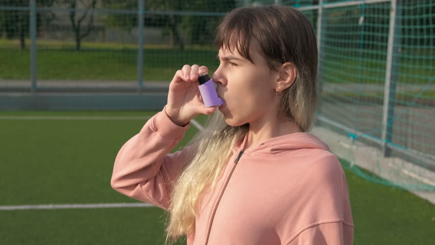 Unwell girl during training. An unhappy teen breathing an inhaler because of asthma attack during sport training.