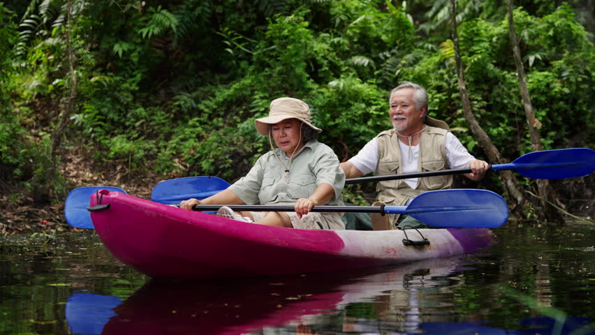 Happy Asian family senior couple kayaking in the river on summer holiday vacation. Healthy elderly people enjoy and fun outdoor active lifestyle travel nature, sport and rowing a boat in the lake.