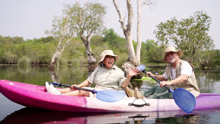 Happy Asian family senior couple kayaking in the river on summer holiday vacation. Healthy elderly people enjoy and fun outdoor active lifestyle travel nature, sport and rowing a boat in the lake.