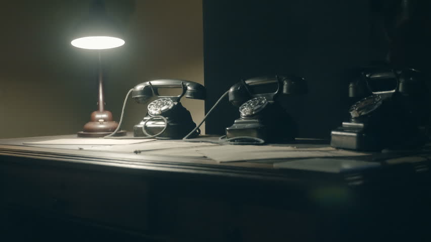 In the semi-darkness there is an old-fashioned Soviet-era table with a lamp, newspapers and black, gloomy rotary telephones. Shot in motion. Translation:"ПРАВДА"-PRAVDA, "Красная Звезда"-Red Star