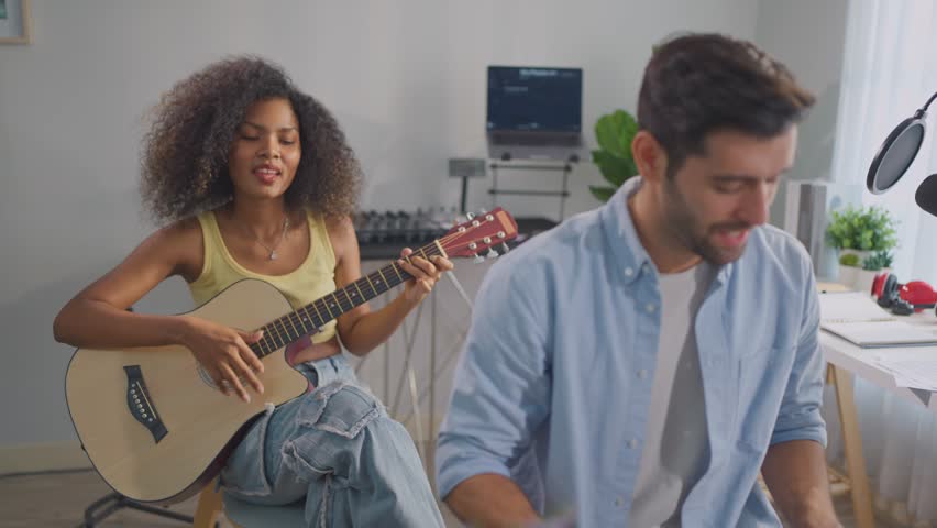 Diverse friend play guitar and produce electronic soundtrack at home. Attractive men and women artist musician composing new song using musical instrument and audio equipment in recording music studio