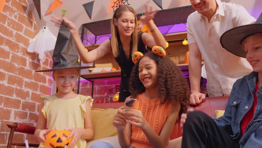 Multiracial family celebrating Halloween party together in house. Attractive parents and their children dressed in Halloween costumes enjoy spend time during holiday festival in living room at home.