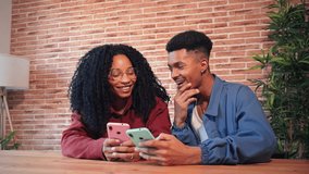 African American couple using their cellphones at home, smiling and sharing moments together, Two friends enjoying technology and connectivity in a cozy, modern living space with brick wall background - Powered by Shutterstock - Get 15% off with code: PIKWIZARD15