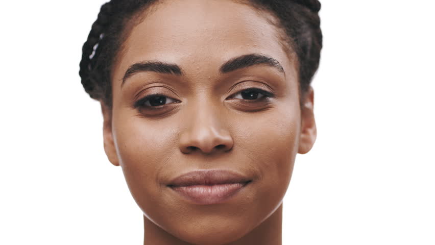 African American young woman displays confidence with her braided hair and calm expression. The neutral background accentuates her features, creating a striking and bold look.