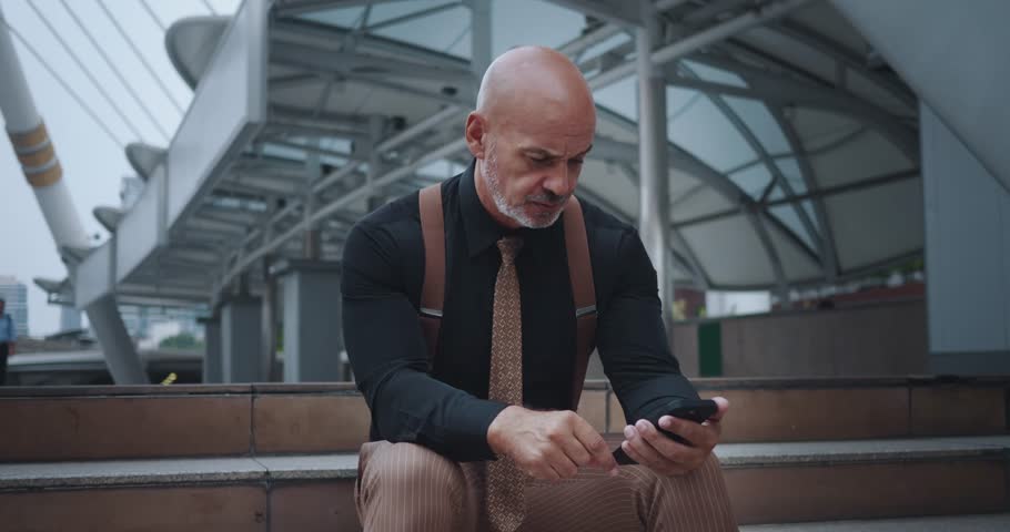 Man sits steps in city, face lit up with joy from what sees screen of mobile phone. Wide smile and animated gestures reveal sincere joy of winning. Man radiates positive energy, rejoicing in victory.