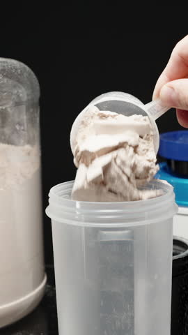 Vertical video. Athlete scooping Protein Powder into the shaker bottle, ready to mix for a post-workout nutrition boost. Slow motion.