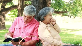 Elderly couple sitting under a tree relaxing in the garden and reading a book, sleeping and leaning against each other happily. - Powered by Shutterstock - Get 15% off with code: PIKWIZARD15