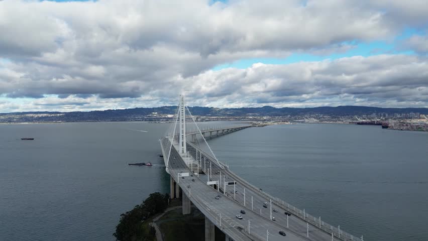 A steady hover drone shot of The Bay Bridge from Yerba Buena Island, CA. The shot captures the bridge and surrounding bay, ideal for showcasing urban landscapes, infrastructure, and travel footage.