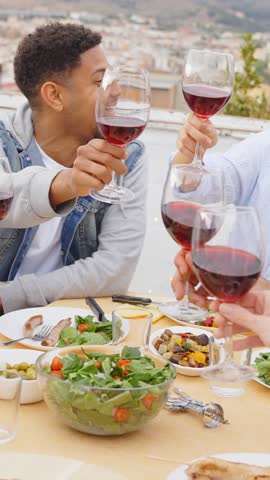 People toasting red wine glasses on rooftop dinner party - Happy friends eating meat and drinking wineglass at restaurant patio - 4k slow motion video