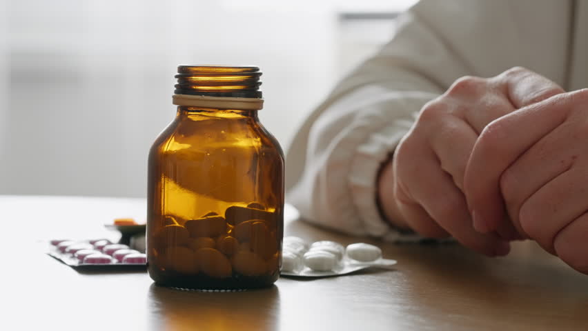 Close-up woman hands pouring white pills from brown bottle. Suggests healthcare, medicine, or supplements, highlighting daily wellness routines and personal health care. Vitamins for women's health