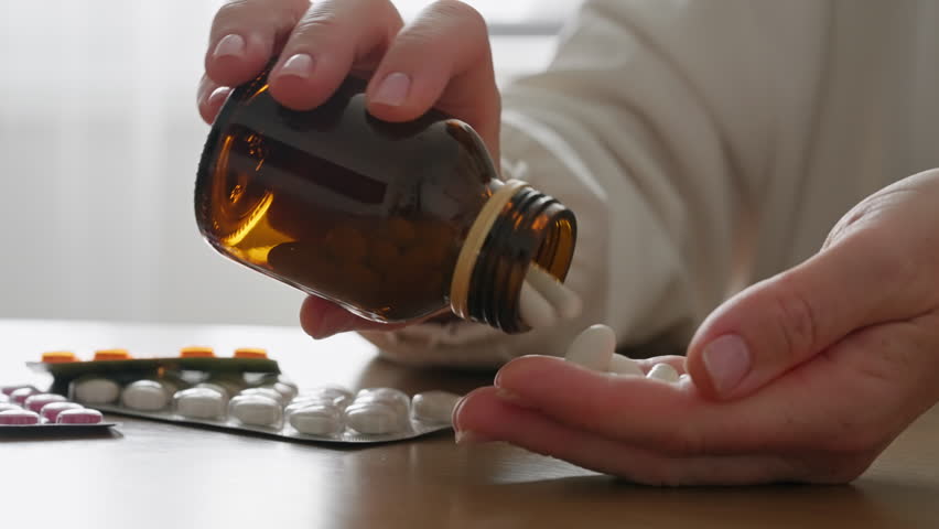 Close-up woman hands pouring white pills from brown bottle. Suggests healthcare, medicine, or supplements, highlighting daily wellness routines and personal health care. Vitamins for women's health