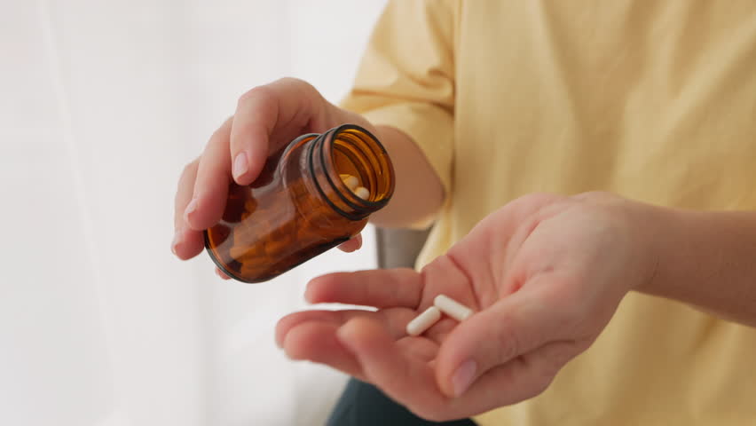 Close-up hands pouring white pills from brown bottle taking pills. Suggests healthcare, medicine, or supplements, highlighting daily wellness routines personal health care. Vitamins for women's health