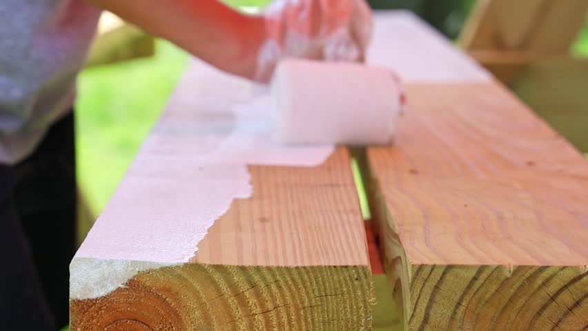 A closeup of workers Painting a wood bench outdoors on a sunny day