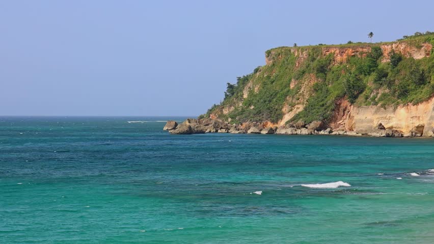 An aerial scene of green cliff by the water in Punta Borinquen Beach on a sunny day in Aguadilla, Puerto Rico