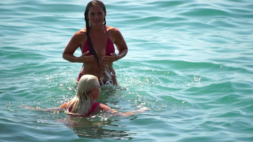 Woman Bikini Beach Water: A woman in a red bikini emerges from the sea on a sunny beach.