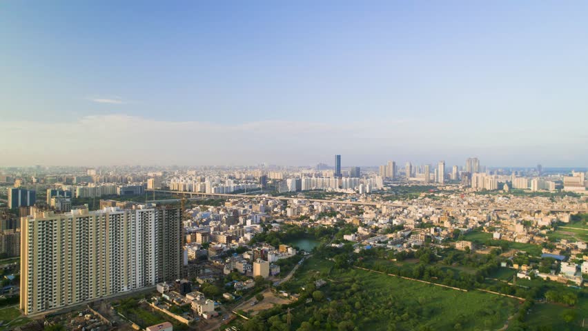 aerial drone shot flying over green grassy field with pond surrounded by skyscrapers multi storey office, apartment, home, malls showing the biodiversity of delhi, gurgaon, noida