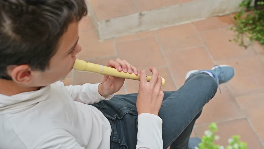 Young boy playing a yellow recorder outdoors on patio
