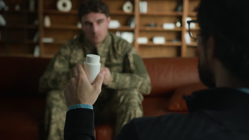 Caucasian mature male man psychologist psychiatrist holding bottle pills painkiller talking about medical drug dose recommending vitamins antidepressants to officer military army soldier indoor clinic