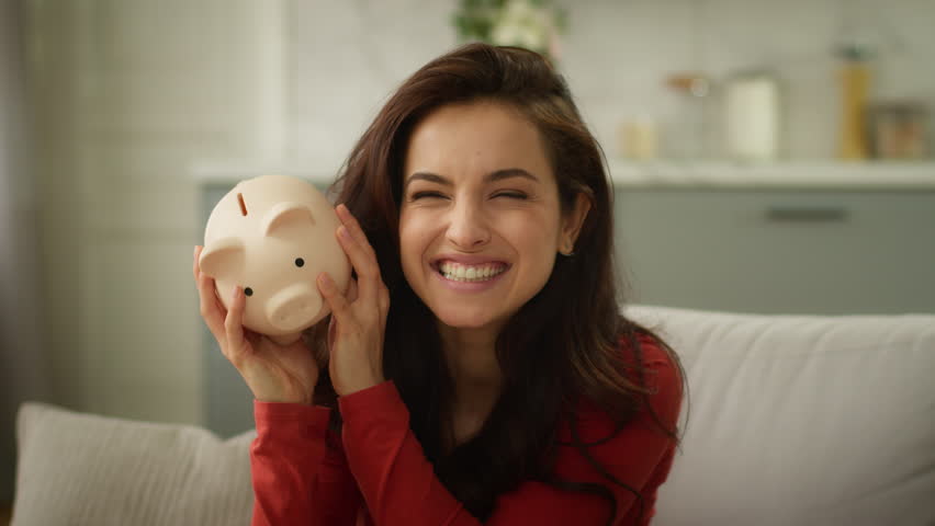 Happy excited laughing Caucasian rich business woman female girl delighted businesswoman shaking piggy bank full of money saving finance wealth cash successful investment deposit currency inside home