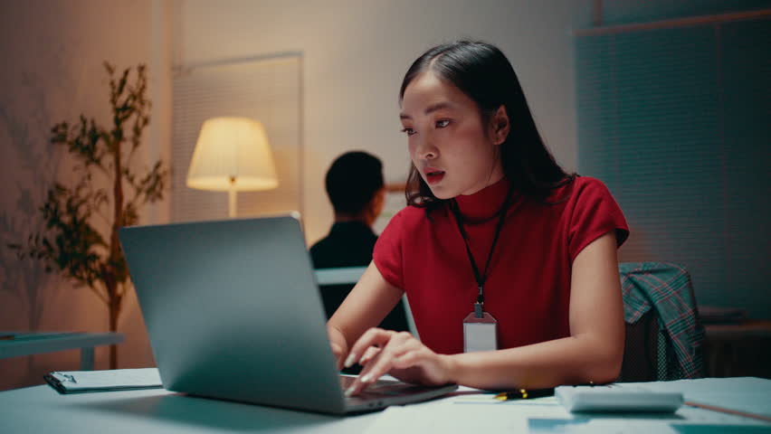 Young professional working late in the office, focusing on her laptop while typing on the keyboard. The atmosphere reflects dedication and ambition in a modern corporate environment