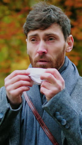Portrait of a handsome young man has a runny nose uses a handkerchief. Sick virus face illness infection allergic. Sneeze. Close up. Slow motion
