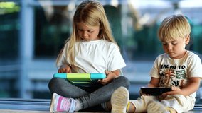 Two young children sitting together using tablets, one smiling at her device, the other focused on his screen. - Powered by Shutterstock - Get 15% off with code: PIKWIZARD15