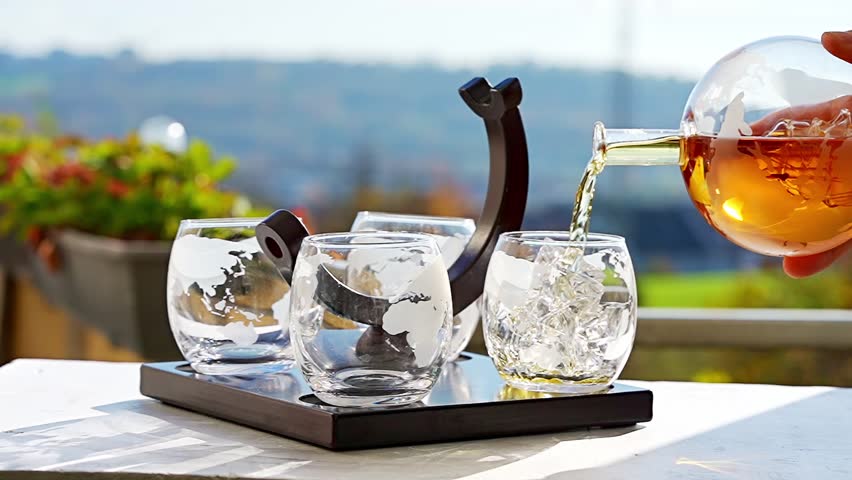 Bartender pours whiskey from a decanter into a globe glass filled with ice, creating a visually appealing display