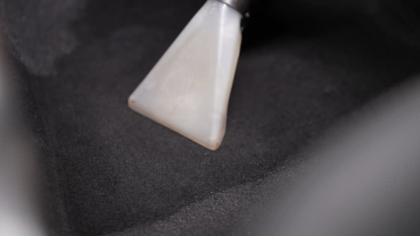 Car wash worker vacuuming wet car carpet with professional vacuum cleaner, removing dirt and restoring interior to pristine condition, demonstrating commitment to exceptional car detailing, closeup.