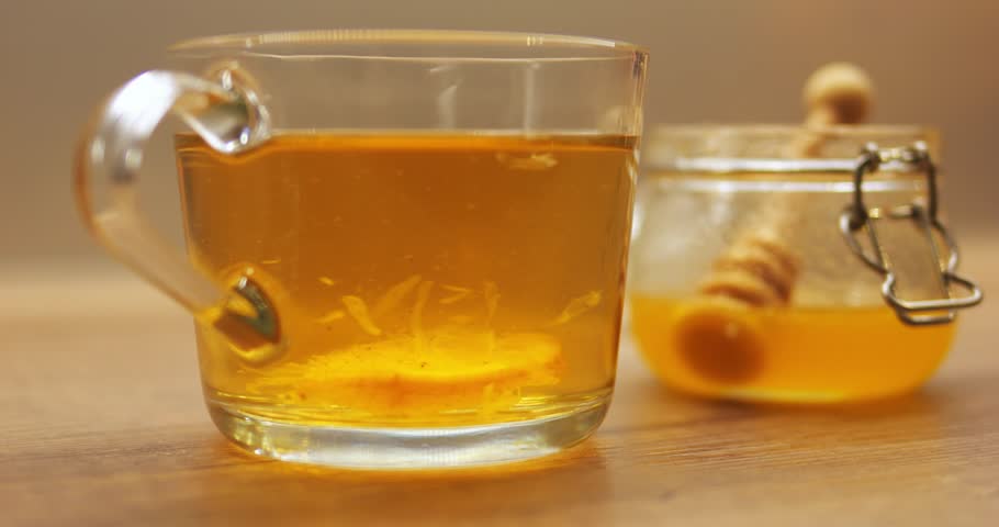 Glass cup of freshly brewed tea featuring lemon slice with organic honey from jar. Hot drink infused with citrus for immune system recharge