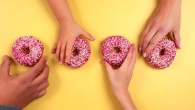 Hands grabbing four pink colorful donuts on light yellow background. Family take delicious donut at same time. Child, Male, Female. Pink glazed with sprinkles. Filmed in Prores, Topview, Slowmotion - Powered by Shutterstock - Get 15% off with code: PIKWIZARD15