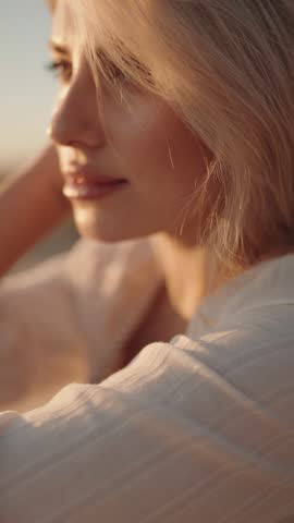 A young blonde woman with closed eyes is bathed in the golden light of sunset. Her serene face embodies peace and tranquility, ideal for themes of relaxation, nature, and beauty.