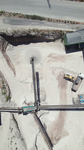 Vertical real-time footage of front loader loading dumper truck with crushed stone. Stone crushing plant top down aerial view. Conveyors, silos and other structures of open pit limestone mine