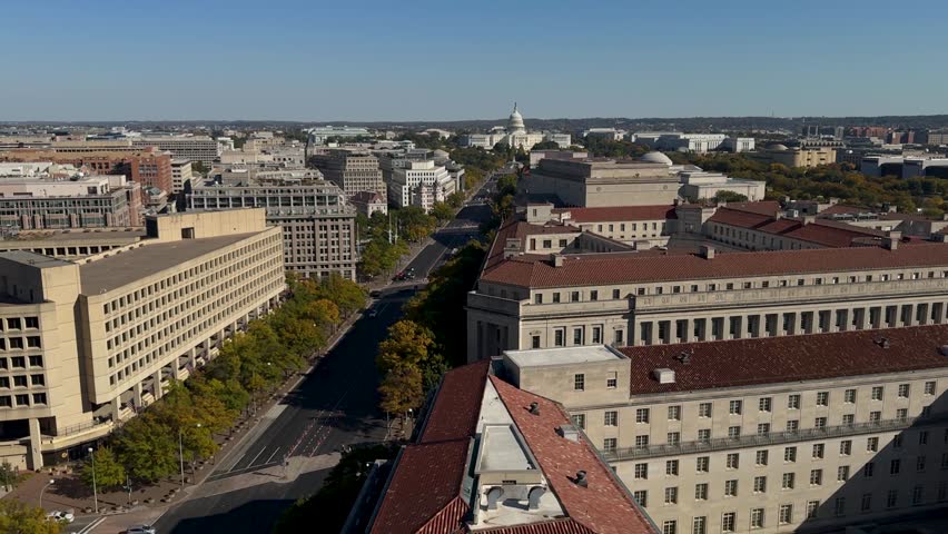 Aerial view of Washington DC featuring a cityscape with various buildings, including the iconic Capitol Building, a street lined with trees, and a large government building with a tiled roof.
