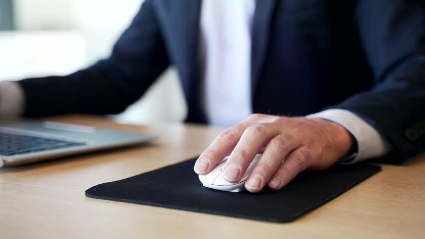 Close up. Office worker holding wrist in pain while using computer mouse. Businessman massages a joint. Concept of ergonomic challenges or repetitive strain injury in a professional work environment