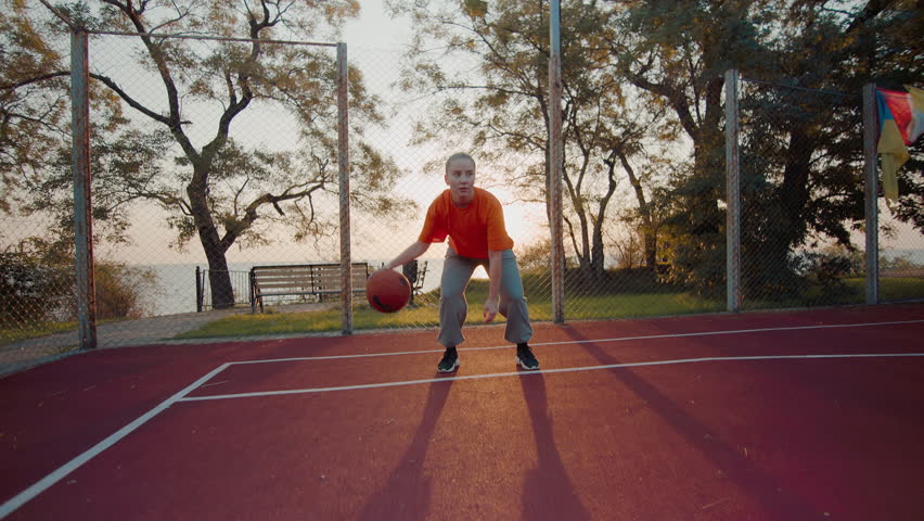 Sporty young woman engages in basketball session at outdoor court on sunny day. Female athlete skillfully bounces ball switching hands smoothly