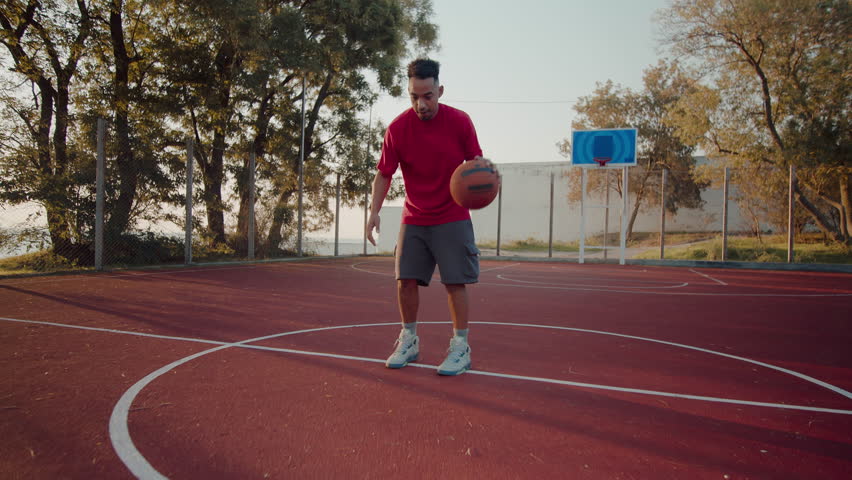 Focused black sportsman bounces ball improving technique for basketball game at outdoor court. Experienced man player shows skills training on weekend