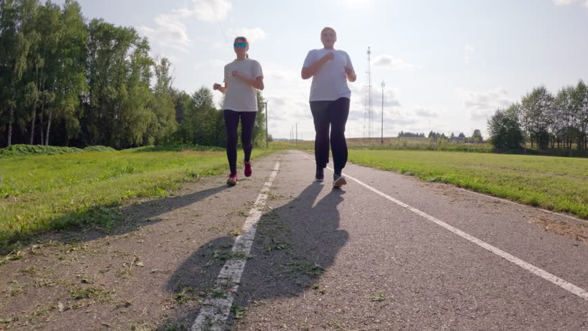 Two women jogging on a sunny paved path showcase their fitness in stylish workout attire, radiating joy and energy during their run