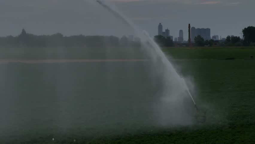 Water cannon sprays green crop field in Netherlands, wide aerial pan