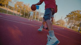Sportive young black man dribbles the ball running along outdoor court with teammates on sunny day. Active people engage in playing basketball game together - Powered by Shutterstock - Get 15% off with code: PIKWIZARD15
