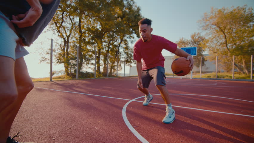 Young sportsmen improve defense technique for playing basketball at outdoor court. Active black man bounces ball trying to block partner stealing ball